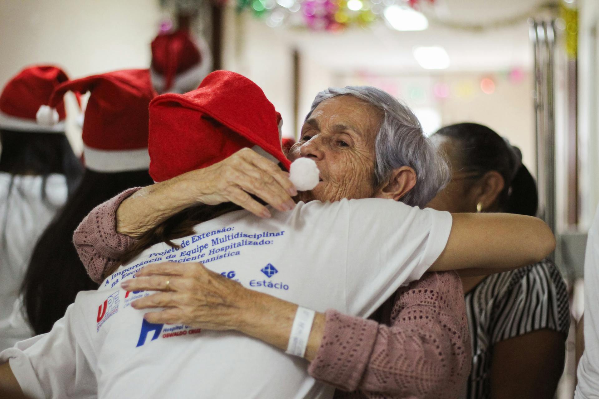 Elderly woman embracing caregiver in festive setting, highlighting companionship and support for seniors in home care services.